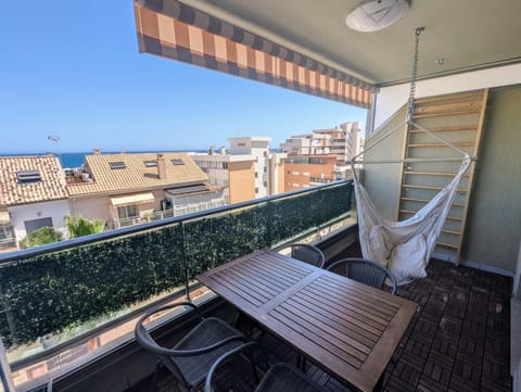 Terrace with hammock, wooden table and awning above the rooftops and the sea
