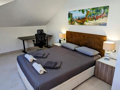 Upstairs bedroom with double bed, sloping ceiling and a desk with ergonomic chair