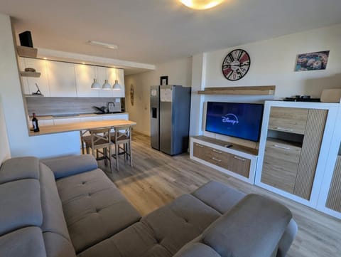 Open-plan living room with corner sofa and smart TV, the kitchen behind